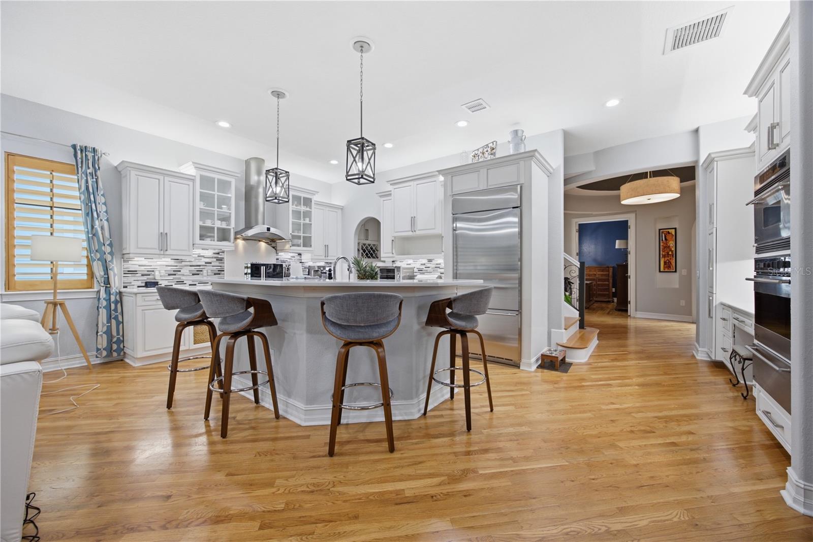 Kitchen with a large island, gray bar stools, white cabinets, and stainless steel appliances.