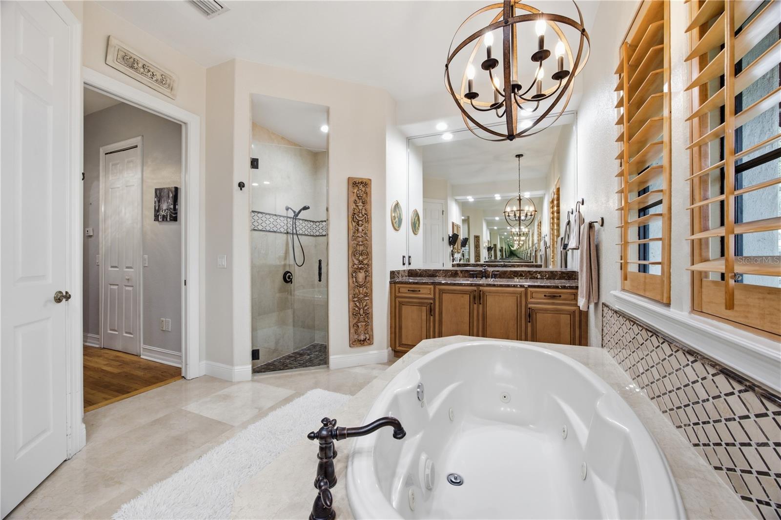 Spacious bathroom with a jetted soaking tub, glass shower, wood vanity, and plantation shutters.