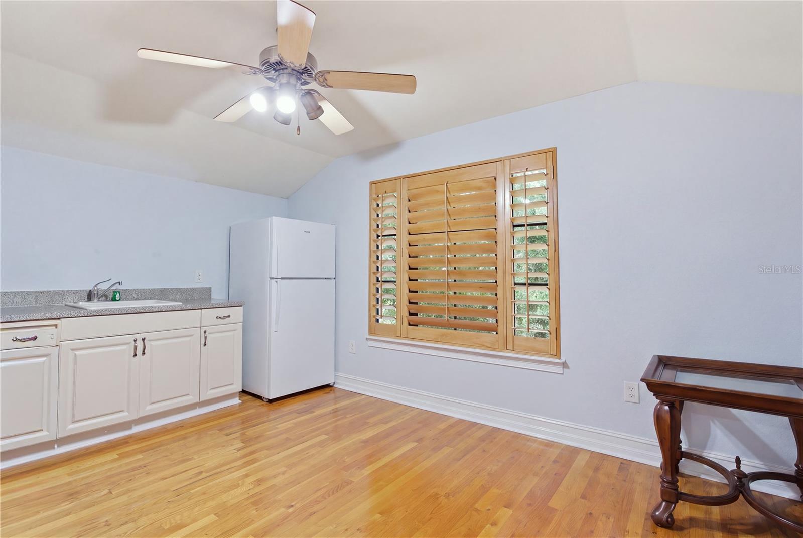 Kitchen with white cabinets, refrigerator, hardwood floors, and a large shuttered window.