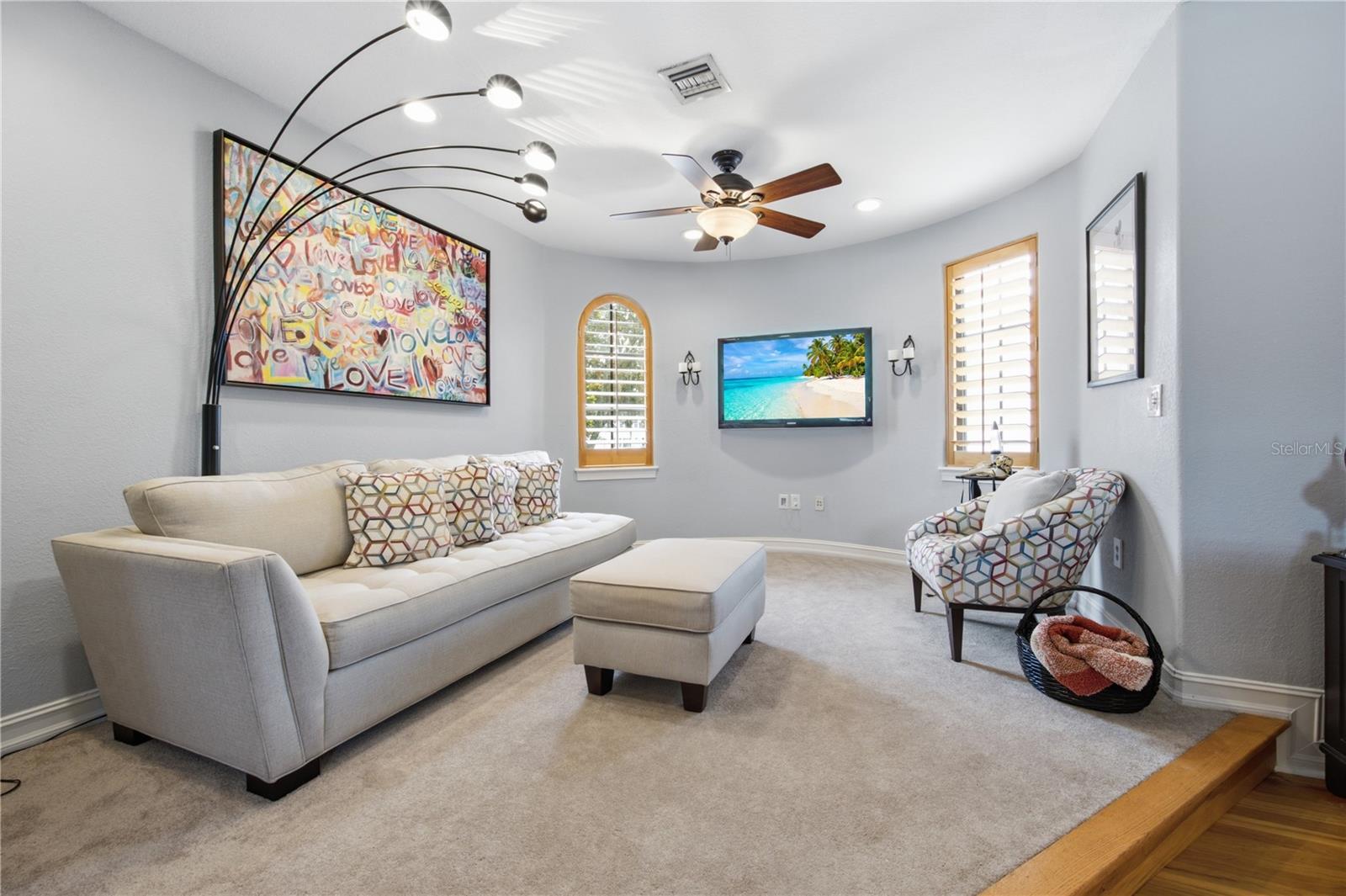 Furnished living room with a cream sofa, patterned chair, wall-mounted TV, and colorful LOVE artwork.