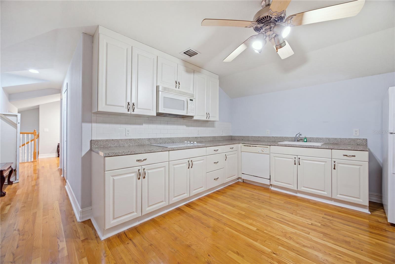 Kitchen with white cabinets, granite counters, and warm hardwood floors.