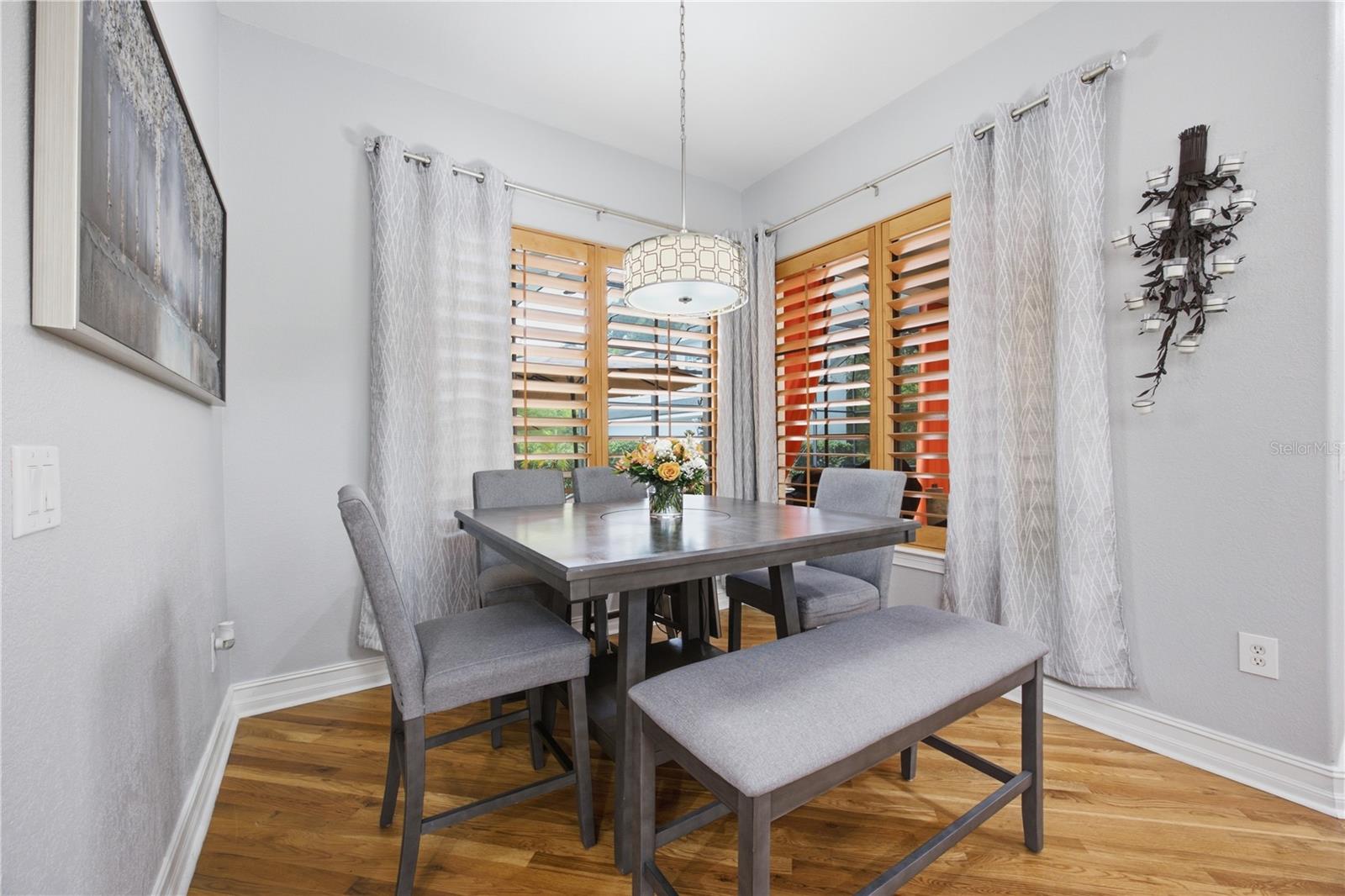 Dining room with a gray upholstered table set, wood floors, and plantation shutters.