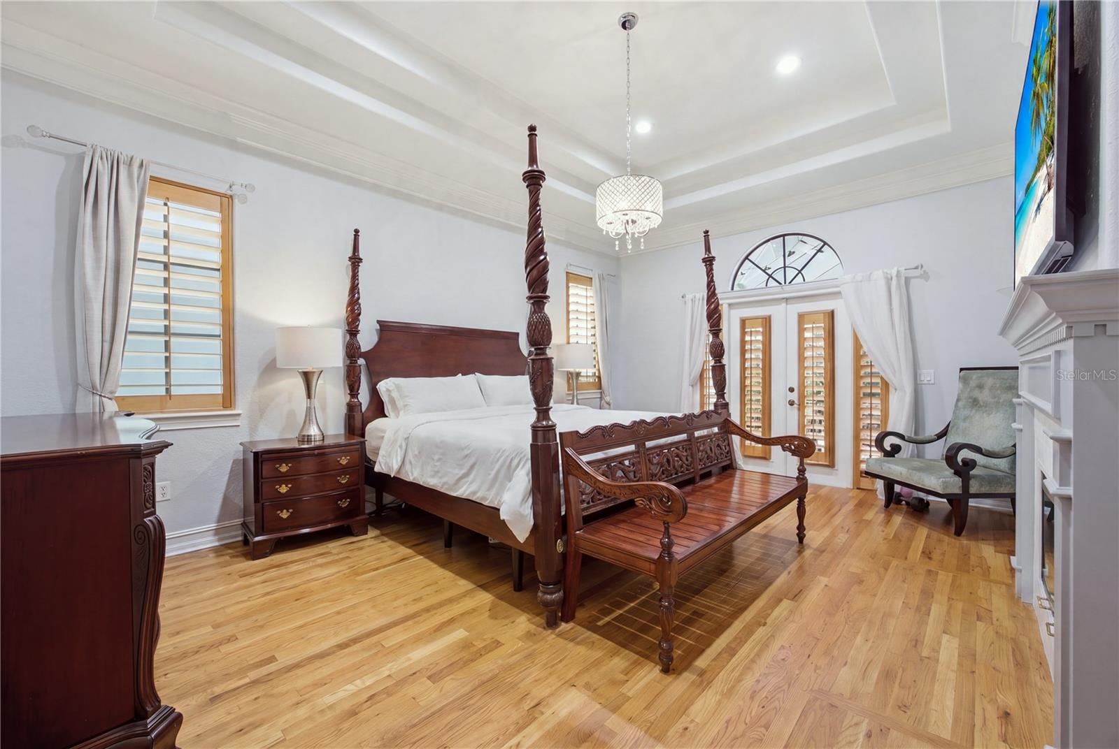 Bedroom with a carved four-poster bed, hardwood floors, and plantation-shuttered windows.