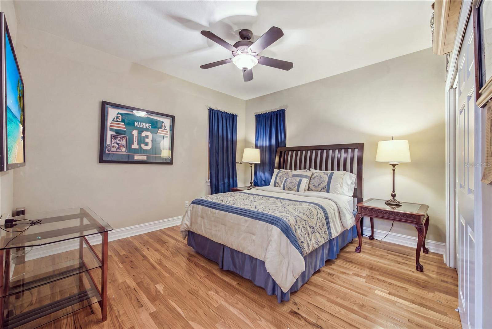 Bedroom with blue-and-white bedding, navy curtains, hardwood floors, and framed sports memorabilia.