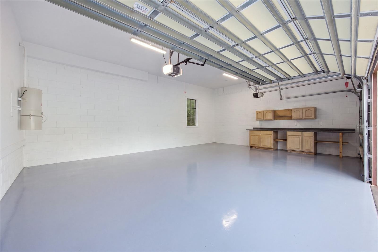 Empty garage with a smooth gray floor, overhead door, and wooden cabinets and workbench.