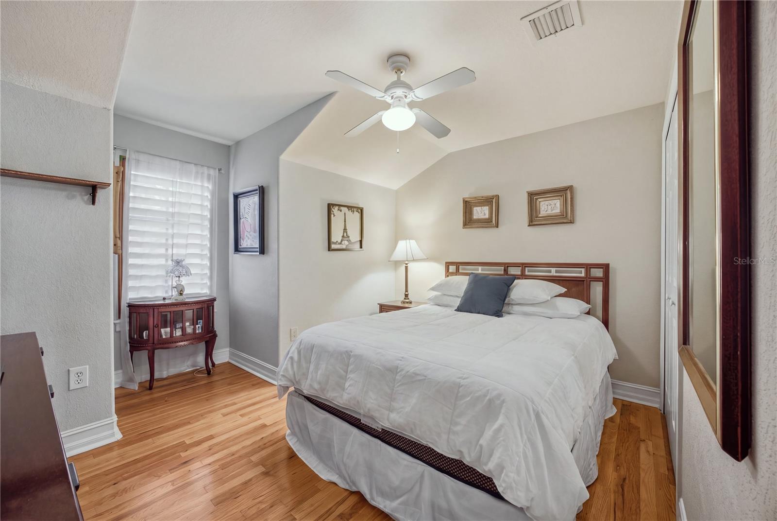 Bedroom with a white bed, vaulted ceiling, ceiling fan, and warm hardwood floors.