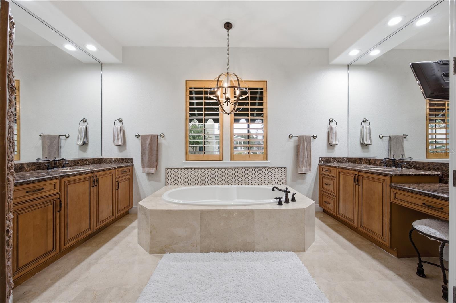 Bathroom with a central soaking tub, mirrored walls, wood vanities, and a shuttered window.