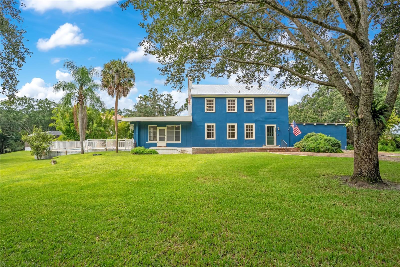 Blue two-story house with a metal roof, broad lawn, and mature trees.
