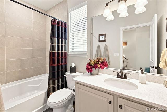 Bathroom with a tub, striped shower curtain, toilet, and light vanity with an oval sink.