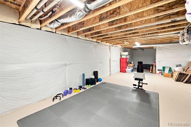 Basement workout area with a gray exercise mat, weights, and exposed ceiling joists.