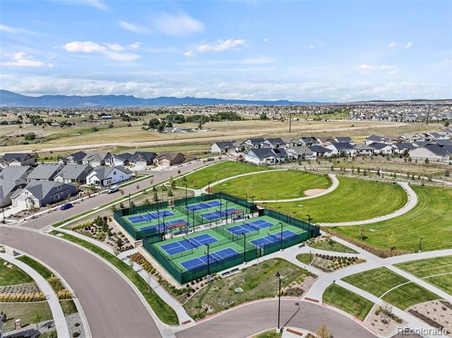 Aerial view of neighborhood tennis courts and park, with homes and mountains beyond.