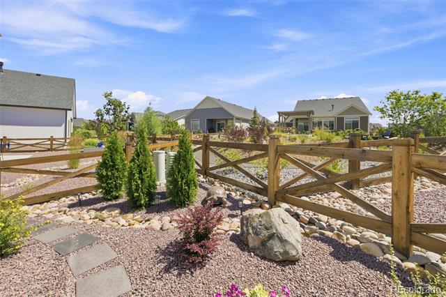 Landscaped yard with gravel, stepping stones, shrubs, and a wooden fence, with homes beyond.