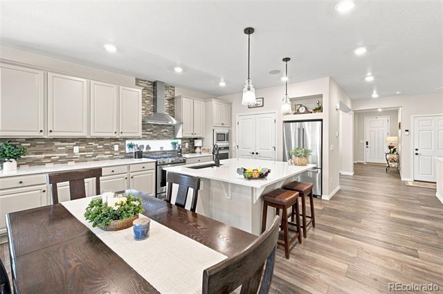 Open-plan kitchen with a large island, white cabinetry, stainless steel appliances, and a dark wood dining table.