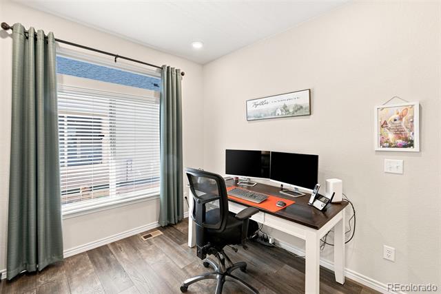 Home office with two monitors, a black office chair, and a large curtained window.