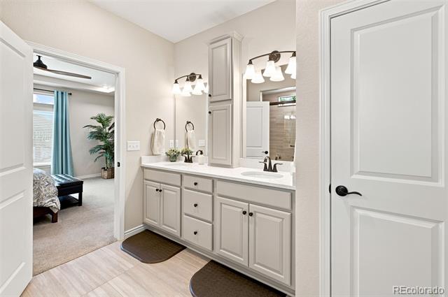 Bathroom with a long double-sink vanity, gray cabinetry, and a doorway to a bedroom.