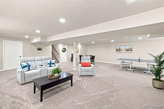 Basement recreation room with gray sofas, a ping-pong table, and light carpeting.
