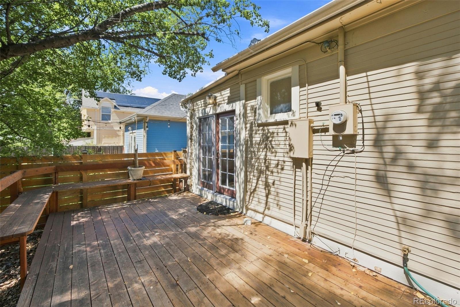 Backyard deck with built-in wooden benches beside a tan-sided house.