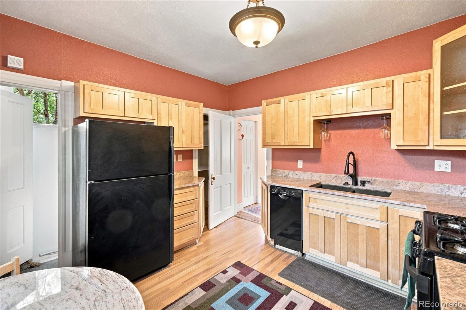 Kitchen with light wood cabinets, red walls, black appliances, and hardwood flooring.