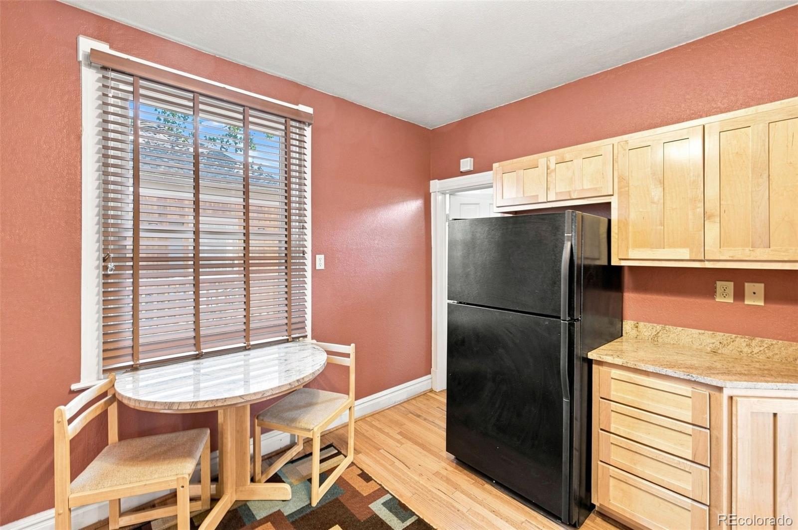 Kitchen with coral walls, light wood cabinets, a black refrigerator, and a round table by the window.