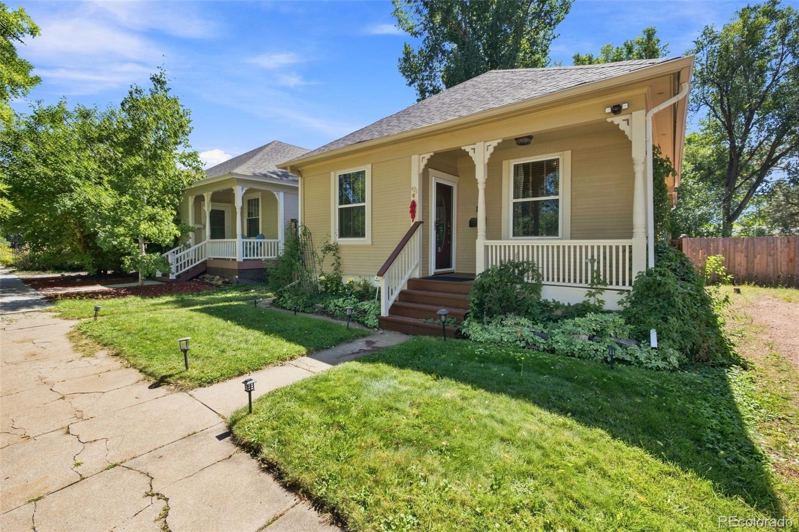 Yellow home with a white-trimmed covered porch, brown steps, and a landscaped front lawn.