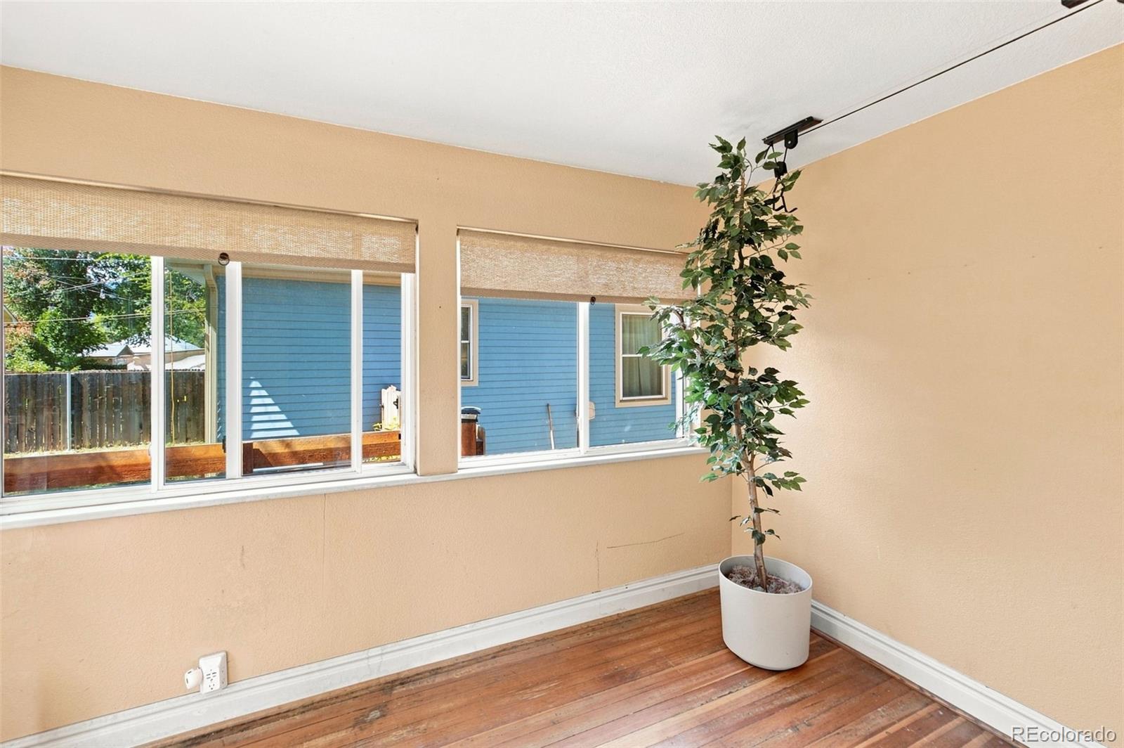 Enclosed porch with wide windows, hardwood floors, and a potted tree.