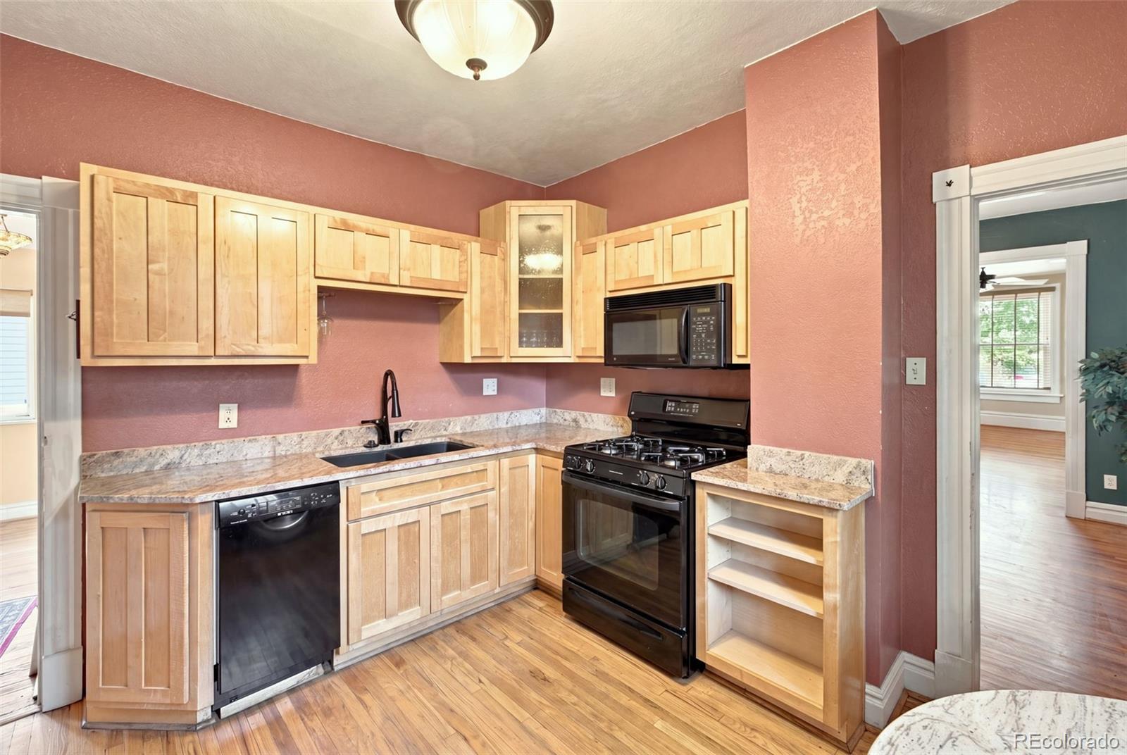 Kitchen with light wood cabinets, granite countertops, and black appliances against dusty rose walls.