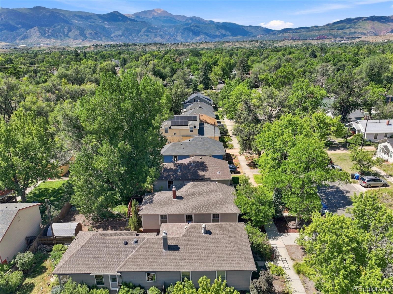 Aerial neighborhood view with tree-lined homes and the Rocky Mountains in the distance.