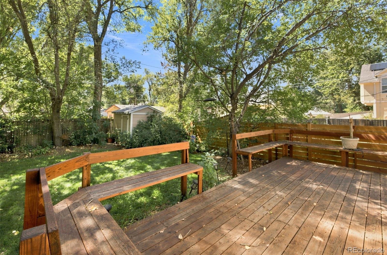 Wooden backyard deck with built-in benches overlooking a leafy lawn and small shed.