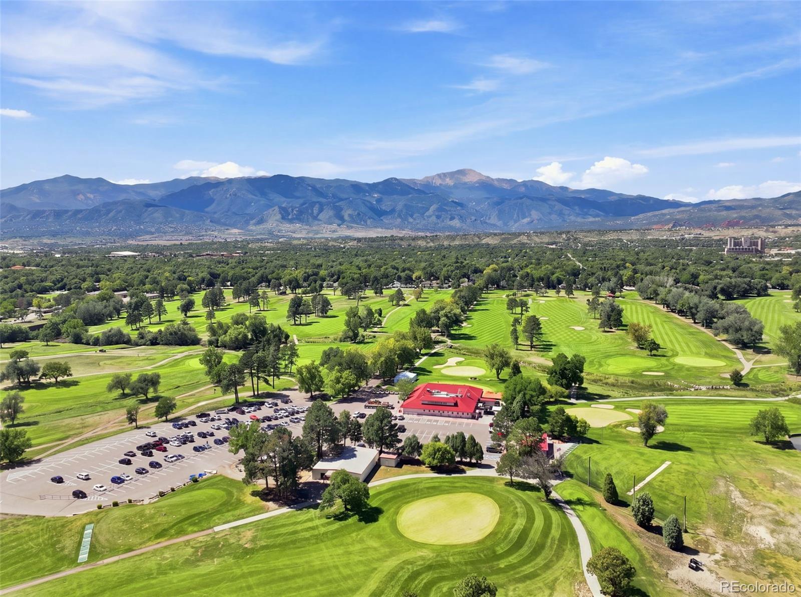 Aerial view of a golf course with a red-roof clubhouse and mountain range beyond.