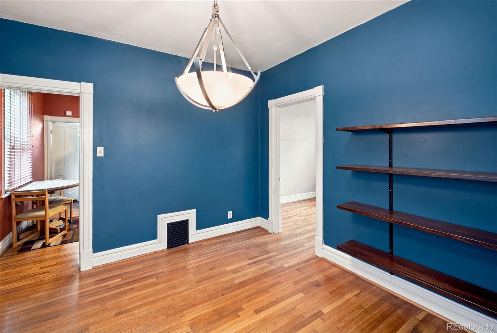 Blue-walled room with hardwood floors, dark wood shelving, and a hanging chandelier.
