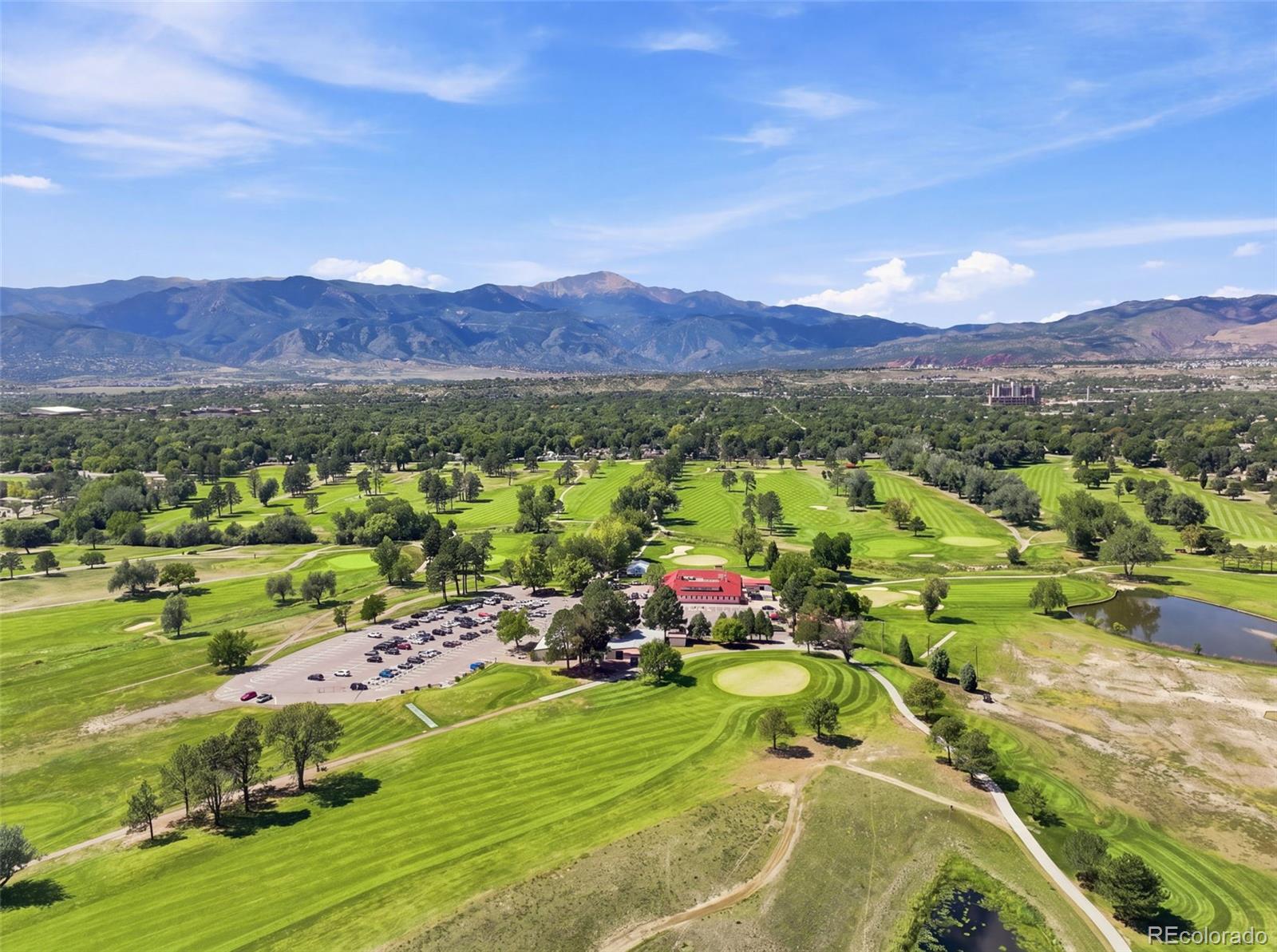 Aerial view of a golf course with striped fairways, ponds, and mountains beyond.