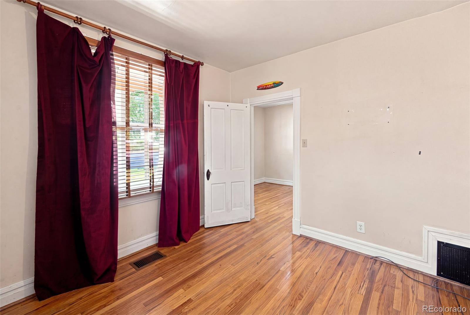 Empty room with hardwood floors, burgundy curtains, and an open doorway.