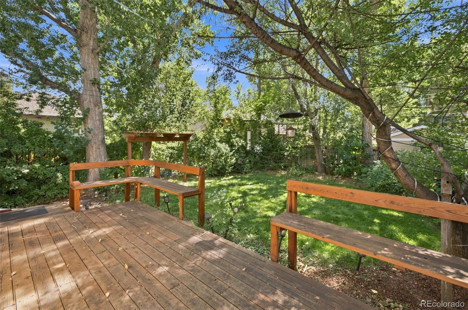 Wooden deck and built-in benches overlooking a shaded, tree-filled backyard.