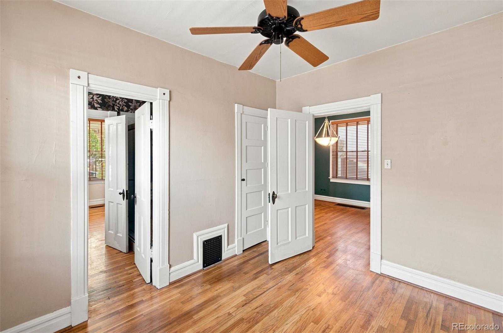 Empty room with polished hardwood floors, white-trimmed doorways, and a wood-blade ceiling fan.