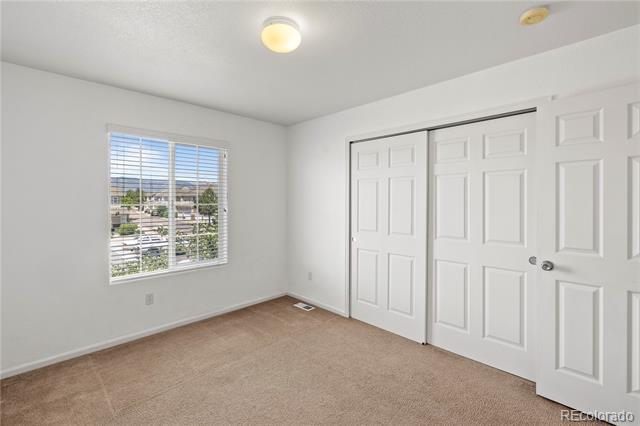 Empty bedroom with beige carpet, a neighborhood view through the window, and white paneled closet doors.