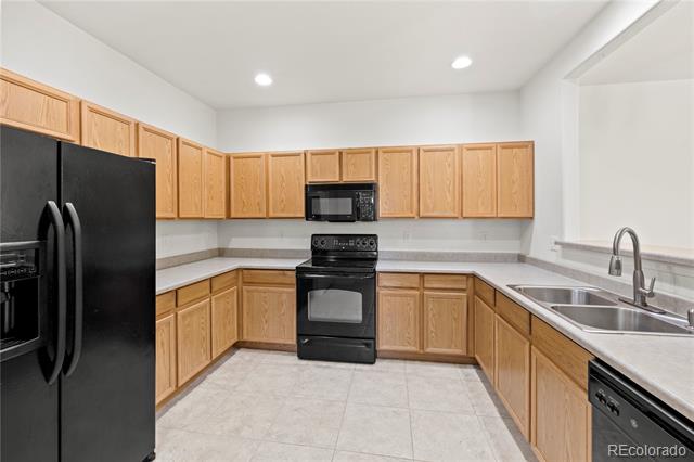 Empty kitchen with light wood cabinets, black appliances, and a double-basin sink.