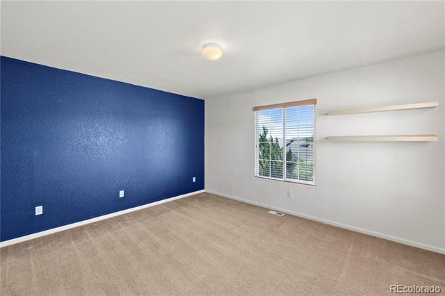 Empty bedroom with a blue accent wall, beige carpet, window blinds, and wall-mounted shelves.
