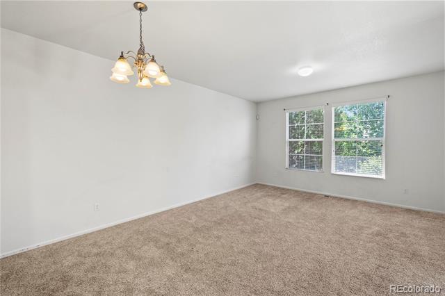 Vacant bedroom with beige carpet, two windows, and a lit chandelier.