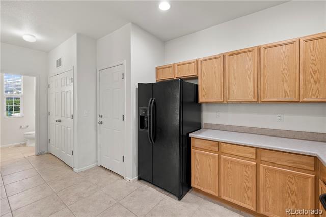 Kitchen with oak cabinets, a black side-by-side refrigerator, and beige tile flooring.