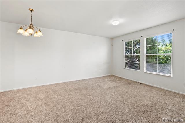 Empty bedroom with beige carpet, two windows with blinds, and a chandelier.