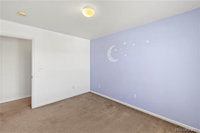 Empty bedroom with a lavender moon-and-stars accent wall and beige carpet.