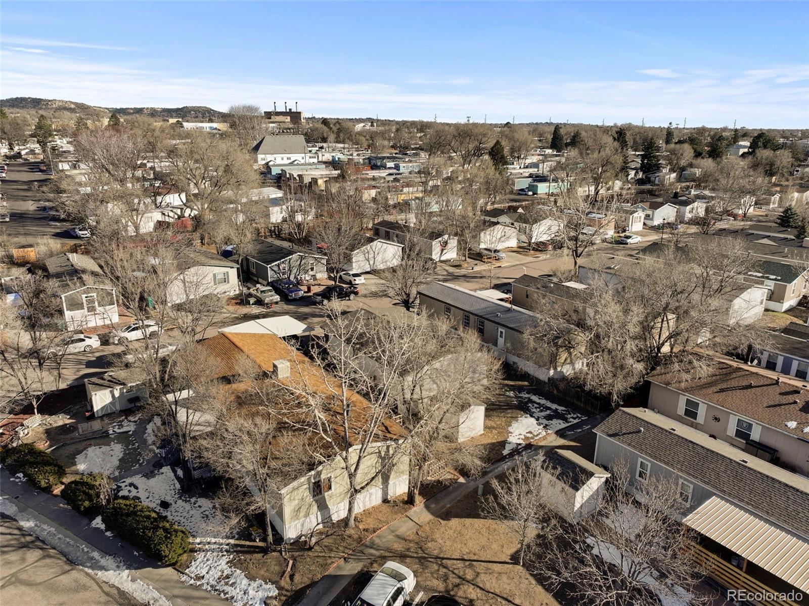 Aerial view of a residential neighborhood with small homes, leafless trees, and scattered snow.