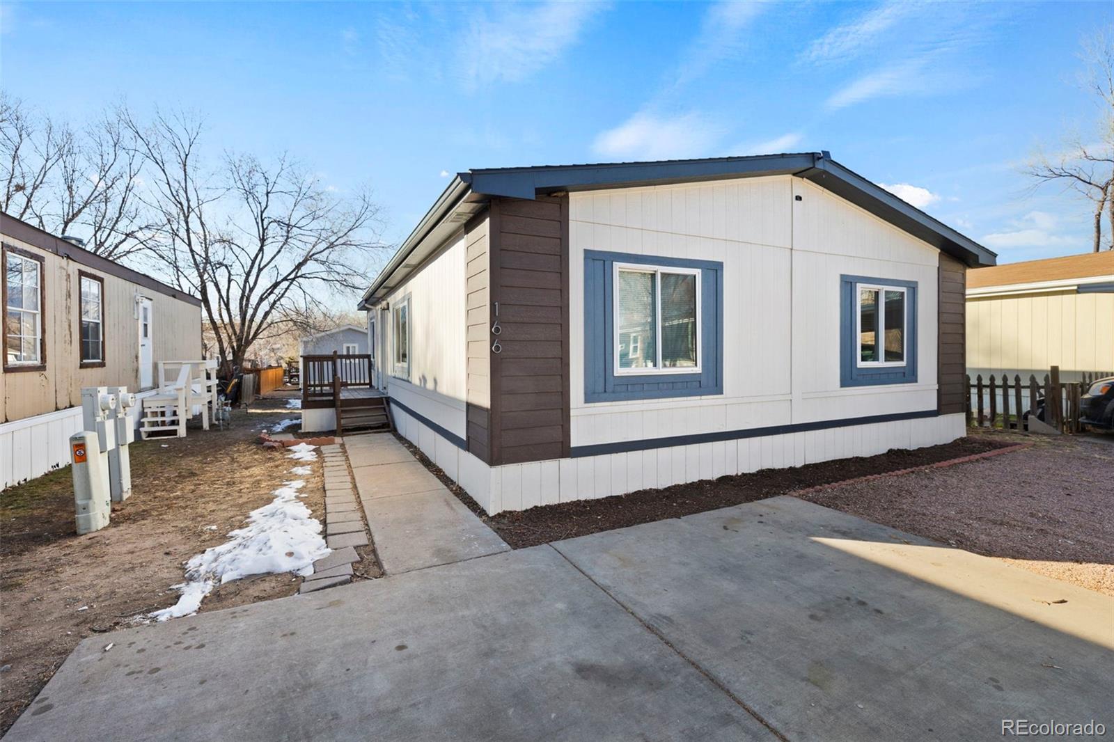 Manufactured home with blue-trimmed windows, brown corner siding, and a concrete walkway.