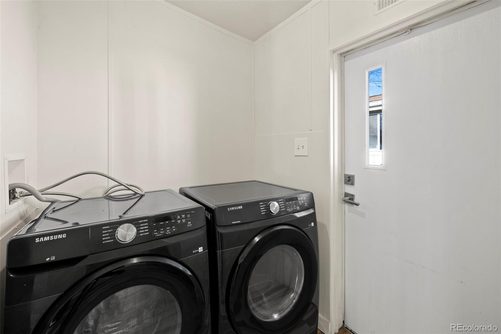 Laundry room with black Samsung front-loading washer and dryer beside a white exterior door.