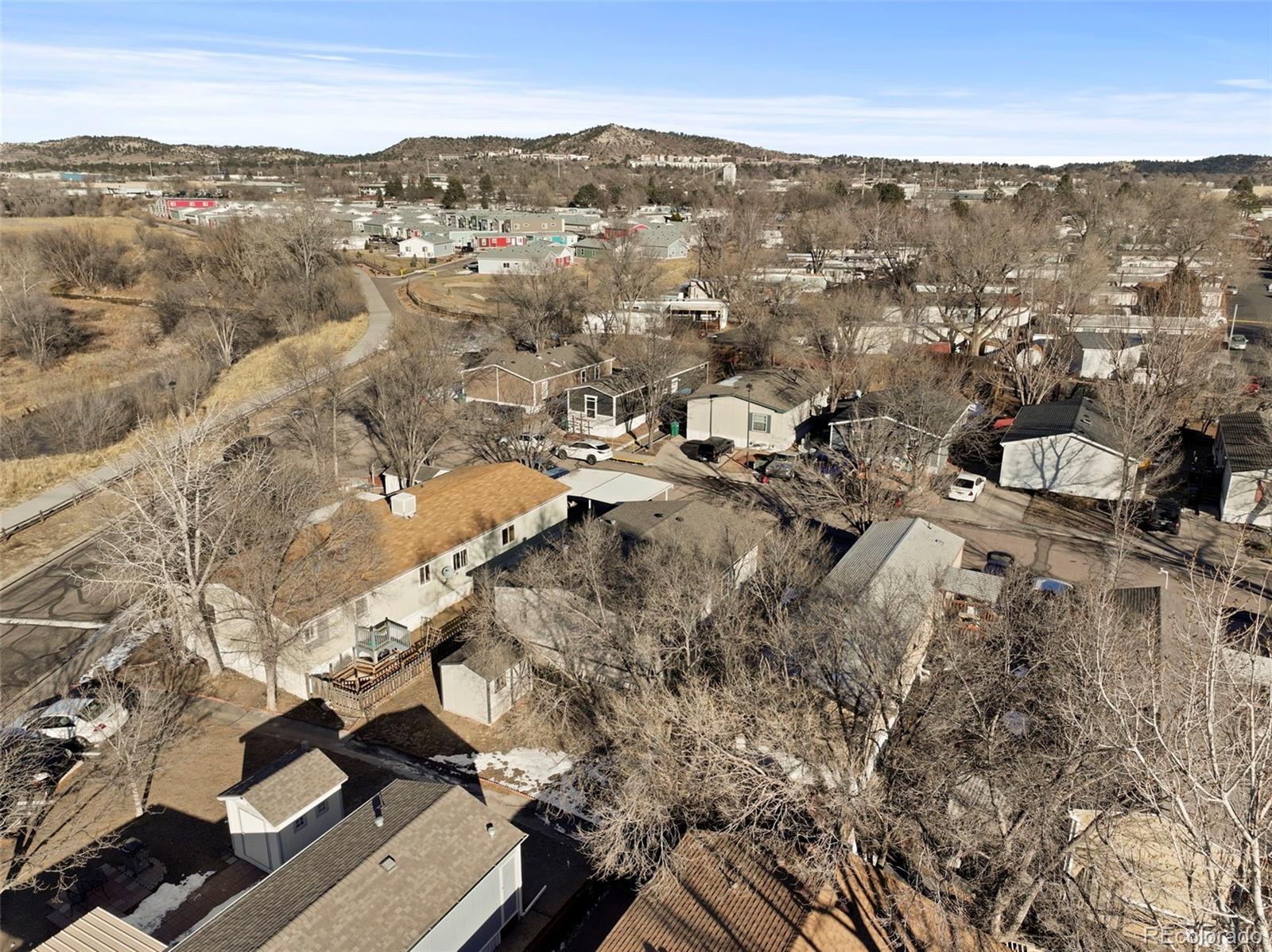 Aerial view of homes and leafless trees, with a winding road and hills in the distance.