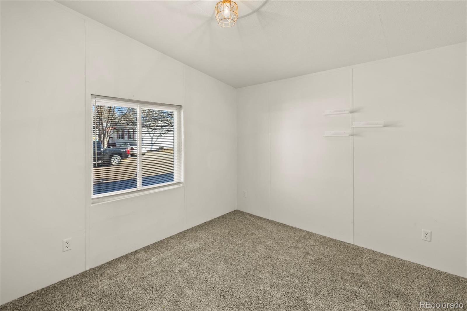 Empty carpeted room with a window, horizontal blinds, and small floating shelves.