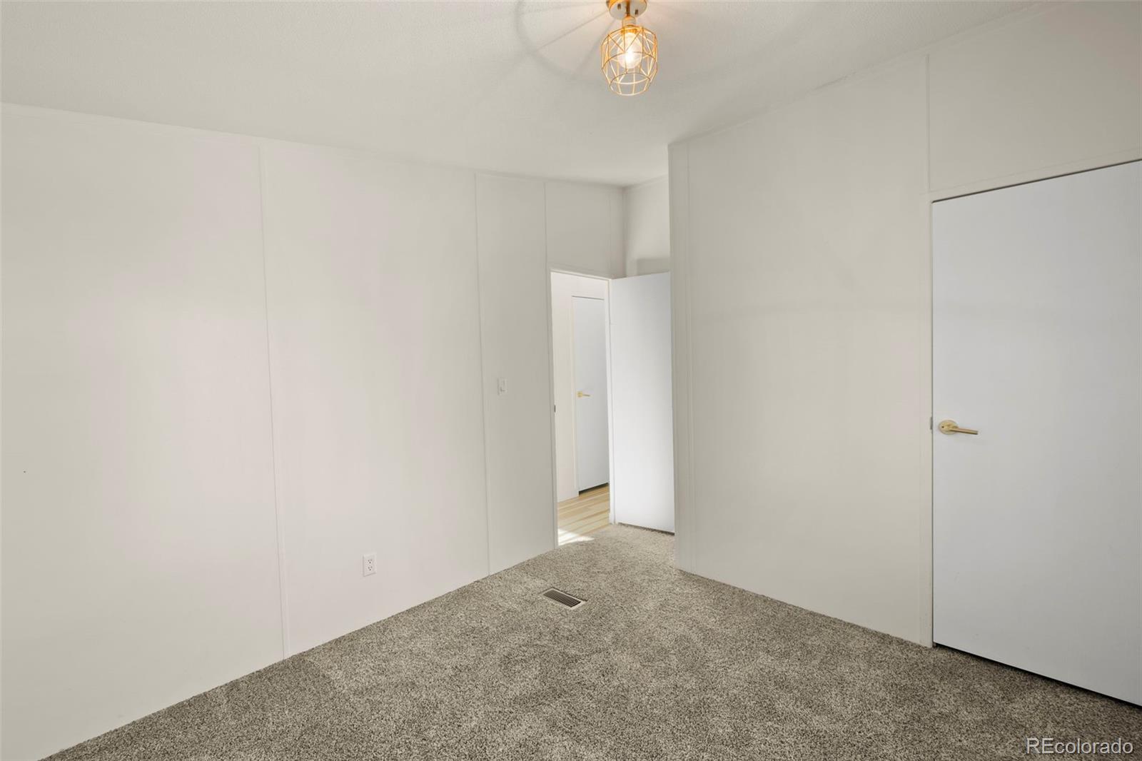 Empty carpeted room with white walls, a geometric ceiling light, and two doors.