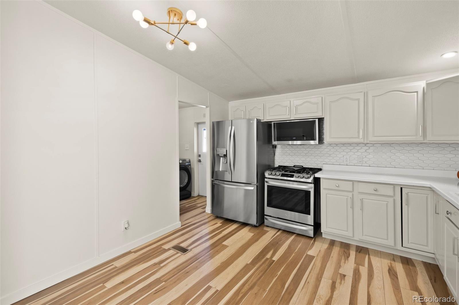 Kitchen with stainless steel appliances, white cabinets, hexagonal tile backsplash, and striped wood floors.