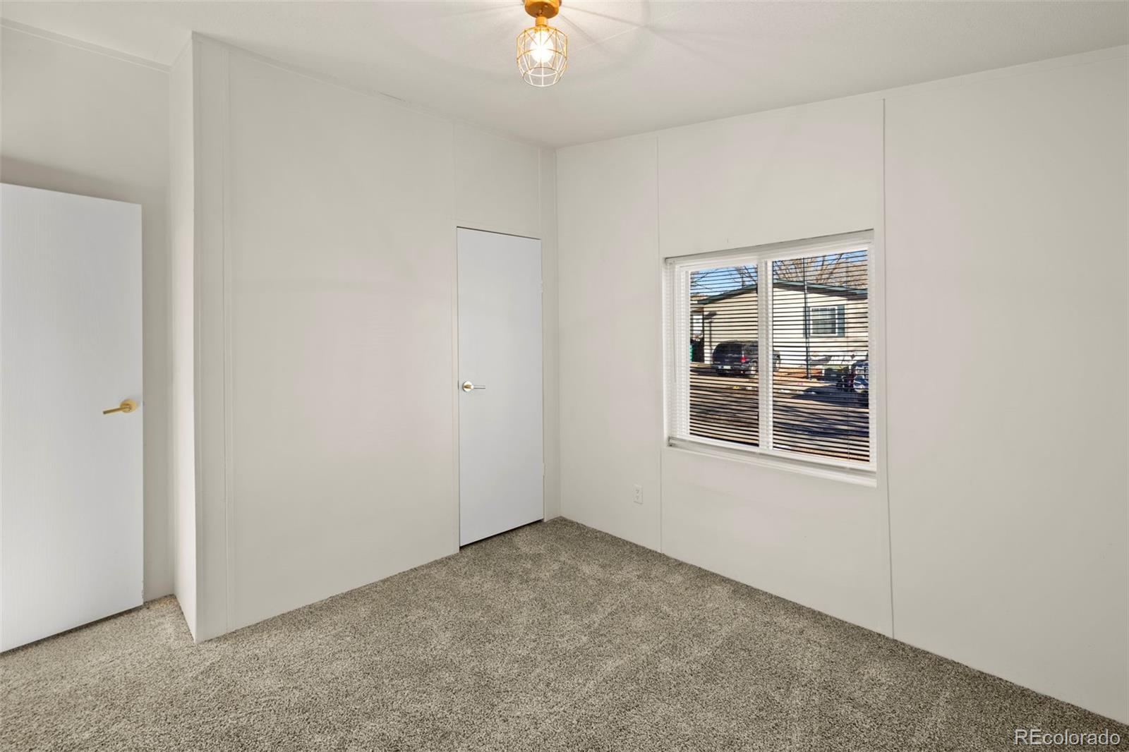 Empty bedroom with beige carpet, white walls, and a window with blinds.
