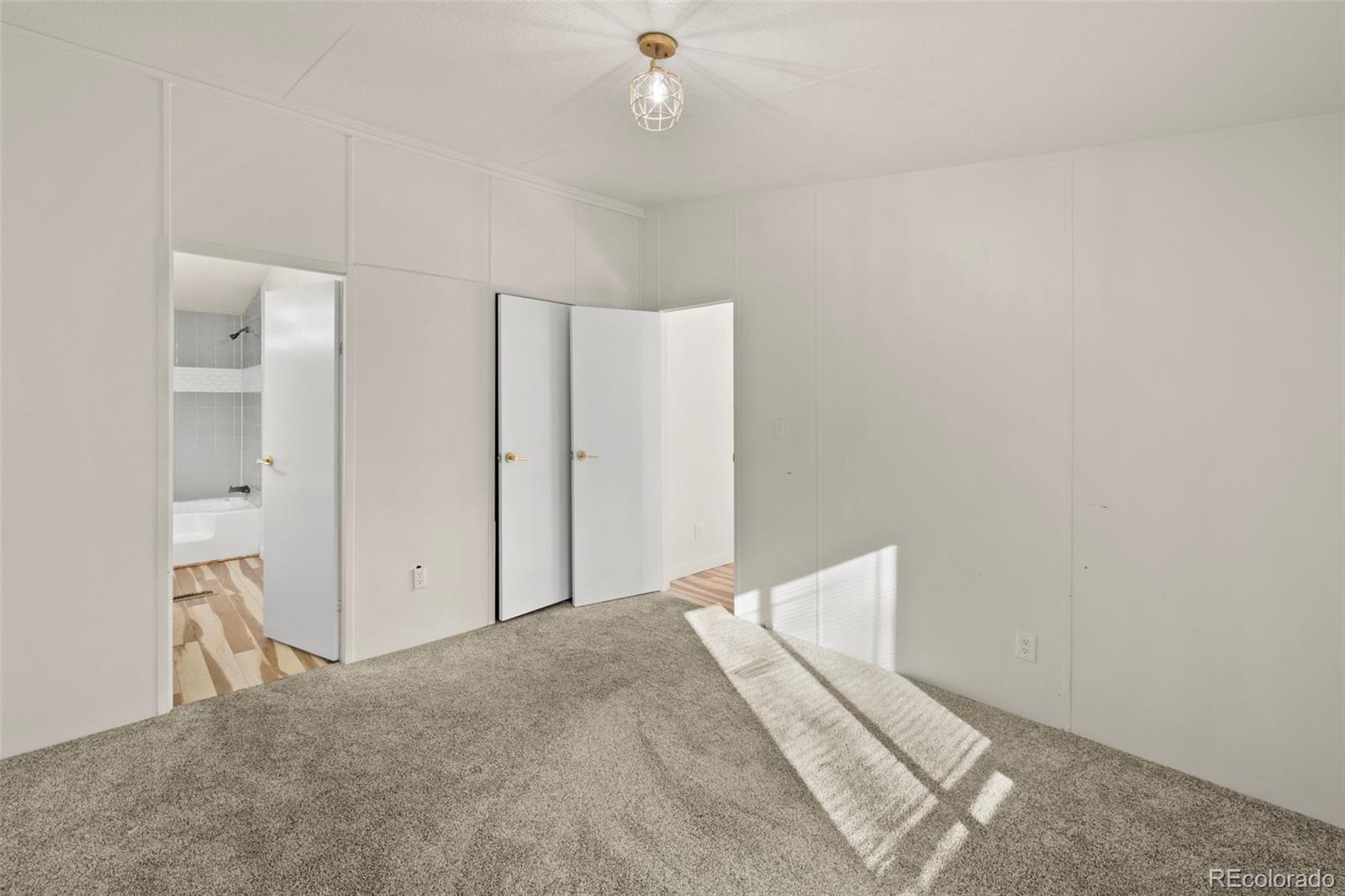 Empty bedroom with gray carpet, white paneled walls, and sunlight cast across the floor.